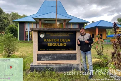 Enumerator survei publik berfoto di depan plang desa lokasi pengumpulan data lapangan