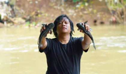 Relawan menangkap ikan sapu-sapu di Sungai Ciliwung dengan latar air keruh Jakarta